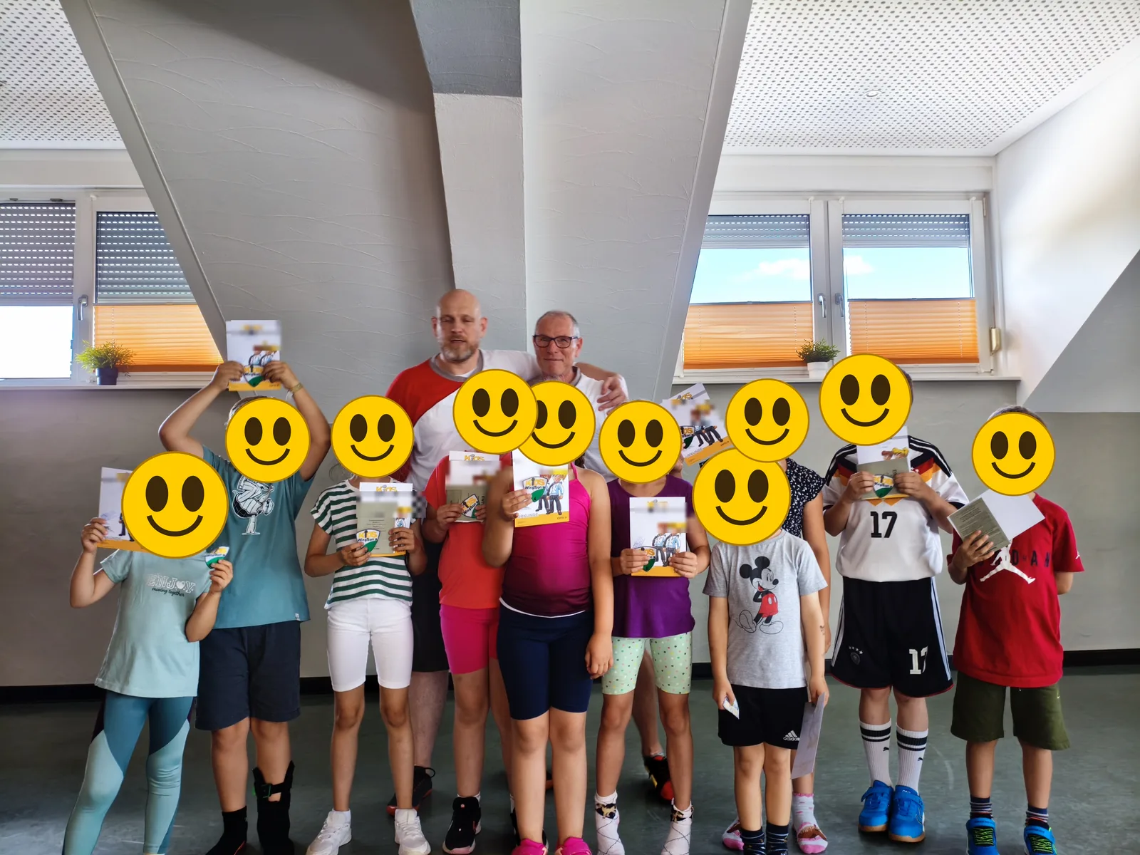 Gruppenfoto nach der bestandenen Schülergradprüfung — die Gesichter der Kinder sind zum Schutz mit Smileys überdeckt